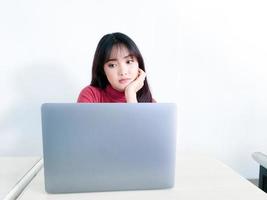 la chica de cabello hermoso asiático está confundida o aburrida en la parte delantera de la computadora portátil en el fondo blanco aislado foto