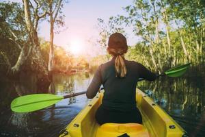 mujer navegando en kayak en el bosque de manglares contra la hermosa luz del sol foto