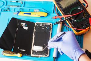 Craftsman in rubber gloves repair or service a mobile phone on a special rubber mat for repair. view from the inside