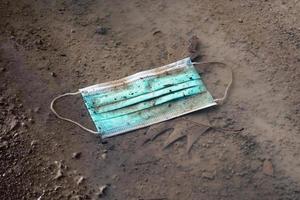 discarded used disposable face mask lying on ground in puddle photo