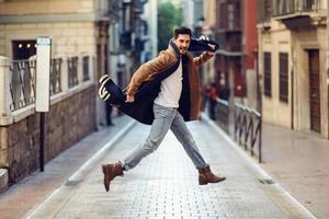 joven hombre feliz saltando con ropa de invierno en el fondo urbano foto