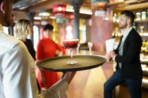 Waiter serving a cocktail for elegant clients in a nice bar photo