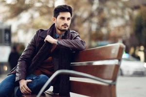 Thoughtful young man sitting on an urban bench. photo