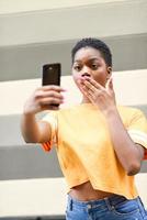 Young black woman taking selfie photographs with funny expression outdoors. photo