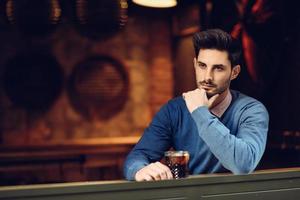 Pensive guy with modern hairstyle near a window drinking a soda. photo