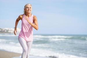 mujer madura corriendo por la orilla de la playa. mujer mayor haciendo deporte para mantenerse en forma foto