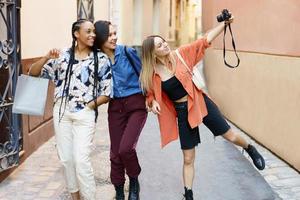 Happy diverse ladies taking selfie on camera during trip in city photo