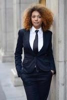 Black businesswoman wearing suit and tie in urban background photo