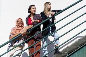 Content young diverse ladies looking away while standing on stairs in city photo
