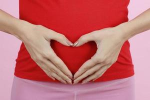 Hands of a mother putting on belly in heart sign or symbol. Concept of love, care and woman awaiting for coming newborn baby. Close-up shot photo