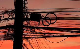 enormes y varios cables y cables eléctricos y de comunicación cuelgan del poste con un fondo desorganizado y confuso en el colorido cielo nocturno foto