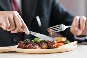 Close up of young businessman eating rib steak on wooden tray at restaurant photo
