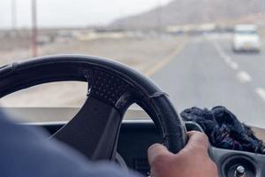 Close up of a man hands holding steering wheel while driving car on the street photo