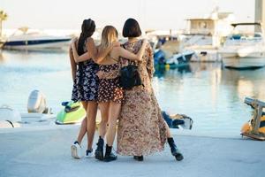 Stylish diverse women hugging on pier with moored boats