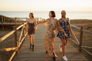 Cheerful diverse girlfriends walking on footbridge near sea