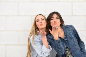 Two young women blowing a kiss on urban wall. photo