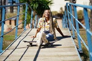 joven negra peinada con trenzas sentada en un puente urbano con una cámara de vacaciones foto