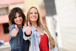 Two young women with thumbs up outdoors photo