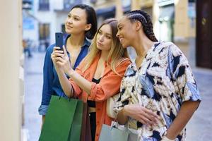 Multiethnic women taking photo of showcase while choosing goods