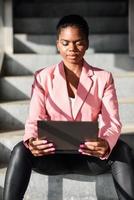 mujer de negocios negra sentada en escalones urbanos trabajando con una computadora portátil. foto