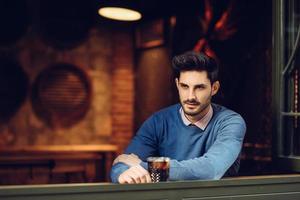 Pensive guy with modern hairstyle near a window drinking a soda. photo