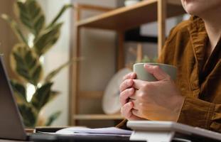 asian woman drink coffee cup and watching live streaming on laptop when work at home photo