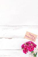 May mothers day concept photography - Beautiful carnations with template card isolated on a bright wooden table, copy space, flat lay, top view, mock up photo