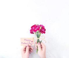 May mothers day idea concept photography - Beautiful blooming carnations tied by rope kraft bow holding in woman's hand isolated on bright modern table, copy space, flat lay, top view photo