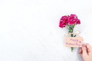 May mothers day idea concept photography - Beautiful blooming carnations tied by rope kraft bow holding in woman's hand isolated on bright modern table, copy space, flat lay, top view photo