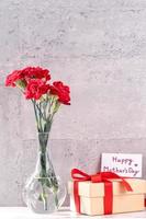 May mothers day handmade giftbox wishes photography - Beautiful blooming carnations with red ribbon box isolated on fair-faced gray background desk, close up, copy space, mock up photo