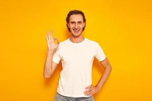 a happy, joyful man in casual clothes shows a sign with his hand ok, everything is fine. isolated on a yellow background with a space for text. concept of people, bargain purchase, vacation photo