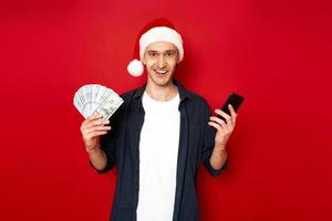 excited man with money and smartphone in hands dressed in Santa Claus Christmas hat rejoices winning lottery, winning, quick cash loan in mobile application. concept - people, technology, finance photo