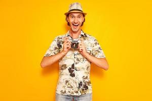 an excited male tourist traveler with his mouth open holds a camera in his hands in front of him. isolated on a yellow background with space for text. concept - people, equipment, vacation, excursion. photo