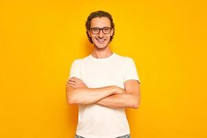confident man with smiling teeth, glasses is dressed in casual clothes crossed his arms on his chest, looks in front of him. isolated on yellow studio background with space for text. concept - people photo