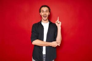excited man with open mouth points index finger up, rejoices in new brilliant idea. dressed in casual clothes isolated on red background space for text. concept - brainstorming, knowledge, inspiration photo
