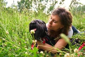 a young pretty girl in a white T-shirt lies on the grass in nature with a black Mittelschnauzer dog and hugs. Space for text. leisure, people, adorable domestic pets concept. love and care for animals
