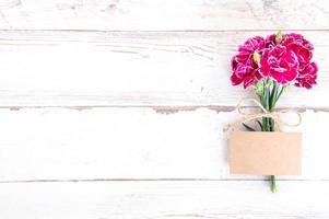 May mothers day concept photography - Beautiful carnations with template card isolated on a bright wooden table, copy space, flat lay, top view, mock up photo