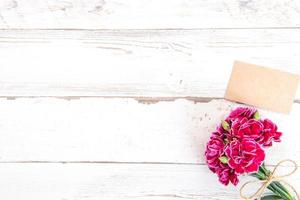 fotografía conceptual del día de las madres de mayo: hermosos claveles con tarjeta de plantilla aislada en una mesa de madera brillante, espacio de copia, capa plana, vista superior, maqueta foto