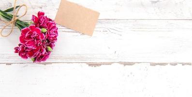 May mothers day concept photography - Beautiful carnations with template card isolated on a bright wooden table, copy space, flat lay, top view, mock up photo