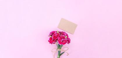 May mothers day idea concept photography - Beautiful blooming carnations tied by bow with kraft text card isolated on bright modern table, copy space, flat lay, top view, mock up photo