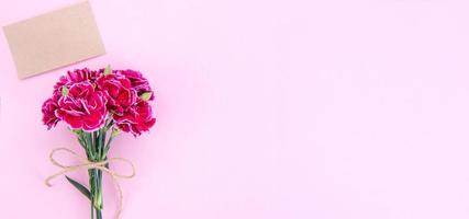 May mothers day idea concept photography - Beautiful blooming carnations tied by bow with kraft text card isolated on bright modern table, copy space, flat lay, top view, mock up photo