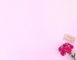 fotografía conceptual de la idea del día de las madres: hermosos claveles florecientes atados por un lazo con una tarjeta de texto kraft aislada en una mesa moderna y brillante, espacio de copia, capa plana, vista superior foto