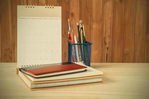 cuaderno, bolígrafo, lápiz y pila de libros con calendario sobre mesa de madera