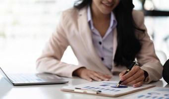 mujer de negocios apuntando con un bolígrafo al gráfico de datos, estimando los beneficios y el estado de resultados de la empresa en el cargo. foto