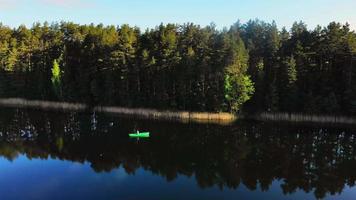 Aerial zoom in view Fisherman with fishing rod fishing in green boat in scenic Lithuanian countryside lake video