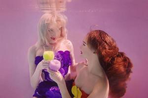 retrato artístico de dos hermosas chicas guapas bebiendo cócteles bajo el agua con fondo rosa foto