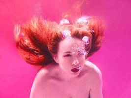 retrato surrealista de una joven mujer atractiva con burbujas de aire bajo el agua en agua colorida con tinta en la piscina foto