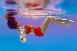 unbelievable, surreal, incredible, amazing underwater portrait of slim, fit woman in bright orange swimming suit photo