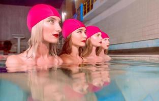 four beautiful amazing slim young stylish women in colorful swimming suits and pink swimming hats in swimming pool photo