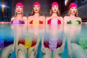 cuatro hermosas y asombrosas jóvenes delgadas y elegantes mujeres con trajes de baño coloridos y sombreros de baño rosas en la piscina foto